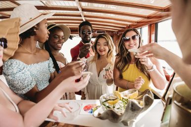 Group of friends on a sunny boat cruise enjoying fresh oysters with lemon over a seafood platter inside a wooden cabin, summer brunch by the ocean