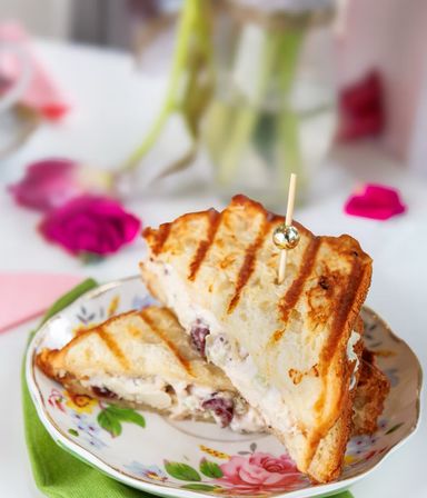 Grilled panini filled with creamy chicken-and-grape salad, skewered with a decorative pick and served on a floral plate for a bright cafe-style brunch.