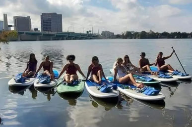 Eight people on stand-up paddleboards relaxing on a calm urban river with a bridge and city skyline in the background