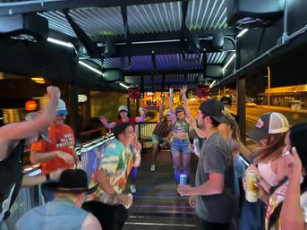 Group of friends dancing and holding drinks on an open-air party bus cruising a downtown street at night