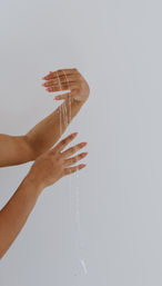 Close-up of hands with pink manicure draping delicate silver necklace chains against a clean white studio background — minimalist jewelry styling photo