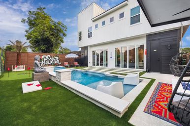 Modern Houston backyard with a rectangular plunge pool and in-pool loungers, artificial turf, Buddha statue, colorful mural and white two-story house with sliding glass doors.