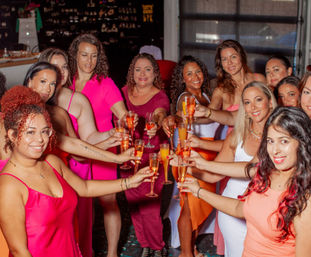Cheerful group of women in colorful dresses toasting with champagne flutes and mimosas at an indoor celebration