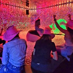 Group of people in pink cowboy hats enjoying a neon-lit indoor ball pit with inflatable ride seats inside a shimmering sequin-walled art installation with colorful LED lights.