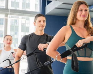 Group fitness class in a bright urban studio: three people doing suspension training with resistance straps, woman in teal activewear in the foreground