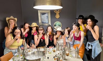 Cowgirl-themed cocktail tasting: a lively group of women sipping drinks around a table with shakers, ice bucket and bar tools in a cozy dining room.