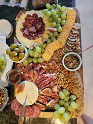 Gourmet charcuterie board with sliced cheese and salami, folded prosciutto, green grapes, fresh figs, round crackers, olives, mixed nuts, honey and olive tapenade