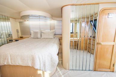 Bright, cozy luxury yacht stateroom with queen bed in cream patterned bedding, mirrored closet panels, light wood cabinetry and curved overhead detail