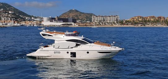 Sleek white motor yacht cruising blue coastal waters past beachfront resorts and hillside condos on a sunny day