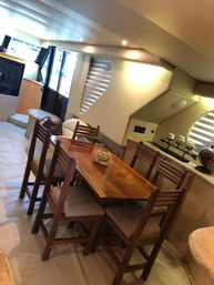 Sunlit yacht interior dining area with glossy wooden table, six cushioned chairs and curved cabin windows