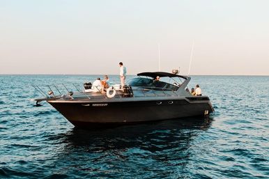 Sleek black motor yacht with people on deck cruising calm blue sea at golden-hour light