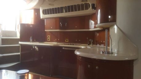 Glossy mahogany yacht galley with cream countertops, curved cabinets, built-in sink and stove, and steps leading to the deck