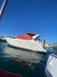 White motor yacht with a red sun canopy docked at a sunny marina under a clear blue sky, hull marked "Loreto, B.C.S.", with rippling water reflections.