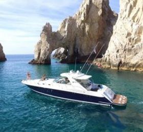 Luxury white-and-navy motor yacht gliding in clear turquoise water beside dramatic coastal rock cliffs and a natural sea arch — scenic boating getaway.