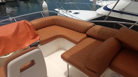 Tan quilted leather lounge seating on a yacht deck at a marina, overlooking docked boats and calm water