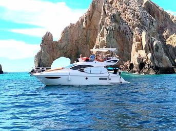 White motor yacht cruising turquoise ocean beside a dramatic rocky sea arch and rugged coastal cliffs under a sunny sky