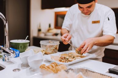 Chef in white uniform spooning colorful appetizer mix onto crispy crackers on a white platter at a kitchen island