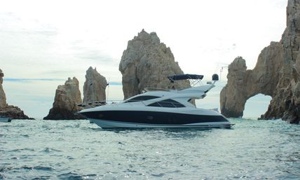 Sleek white-and-navy motor yacht cruising past dramatic coastal rock formations and a natural sea arch on turquoise ocean under a pale sky