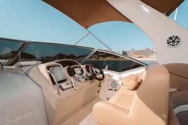 Sunlit motor yacht helm with tan leather captain’s chair, steering wheel, navigation instruments and VHF radio, overlooking a calm marina and distant coastline
