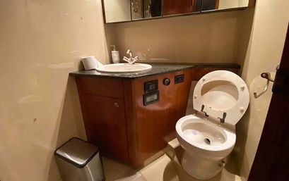 Cozy compact bathroom with a white toilet, wood vanity with black countertop and round sink, mirrored cabinet and small stainless trash bin