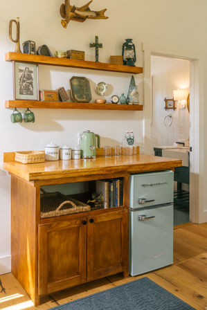 Sunlit cozy farmhouse kitchen coffee station with wooden countertop, open shelves of vintage decor and a mint retro mini fridge
