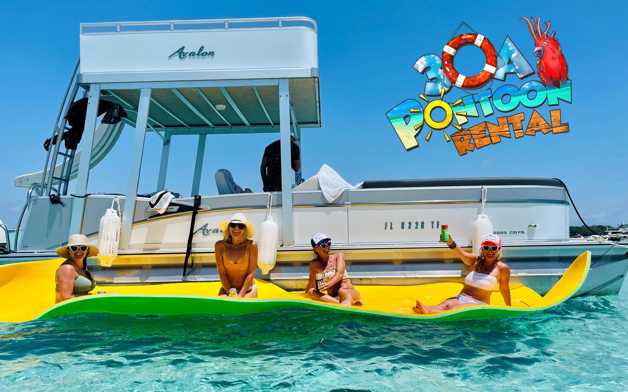 Four women in swimsuits and sun hats lounging and smiling on a bright yellow floating mat beside a white pontoon boat in clear turquoise coastal water on a sunny day, one holding a drink.