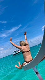Woman leaping from a boat slide into crystal-clear turquoise ocean with a motorboat and sunny blue sky in the background