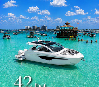 White 42-foot cruiser anchored in crystal-clear turquoise water near a lively sandbar with a floating tiki bar and dozens of boats under a bright blue sky