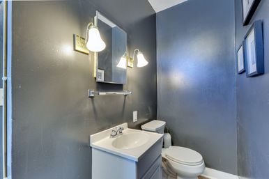 Compact residential powder room with dark gray walls, white vanity sink, wall-mounted mirror, two lit brass sconces, and a white toilet.