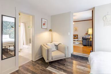 Cozy modern apartment interior with a beige armchair reading nook, wood-look floors, bathroom doorway, and living room view