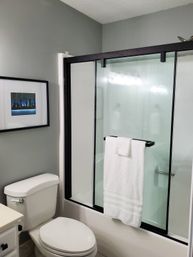 Contemporary residential bathroom with gray walls, black-framed sliding glass shower, white towel on the bar, white toilet, and framed skyline art