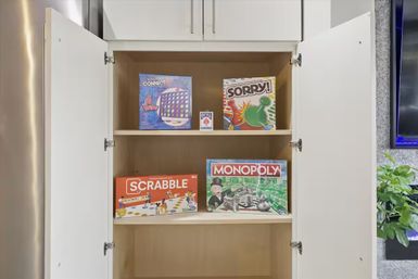 Open white cabinet in a family room displaying board games for game night — Scrabble, Monopoly, Sorry!, Connect 4 and a deck of cards.