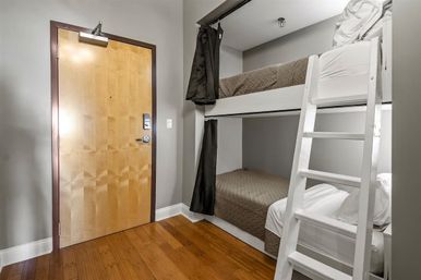 Cozy modern bunk-bed room with white ladder, privacy curtains, gray walls, hardwood floor, and wooden entry door.