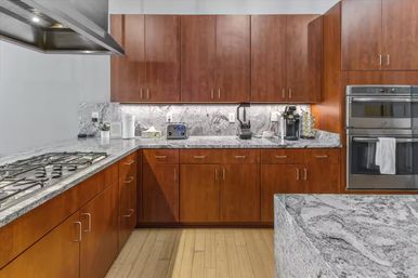 Sleek modern kitchen with warm wood cabinets, gray granite countertops and island, gas cooktop, stainless double wall ovens and a coffee station.