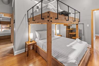 Cozy loft-style bedroom featuring a sturdy wooden double bunk bed with white linens, bedside lamps, hardwood floors, and gray walls