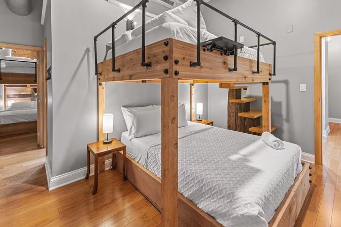 Cozy loft-style bedroom featuring a sturdy wooden double bunk bed with white linens, bedside lamps, hardwood floors, and gray walls