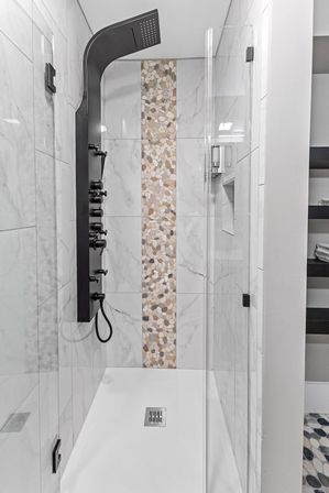 Sleek walk-in shower with matte black multi-jet shower panel, vertical pebble-mosaic accent strip, white marble-look wall tiles and frameless glass door in a modern bathroom.