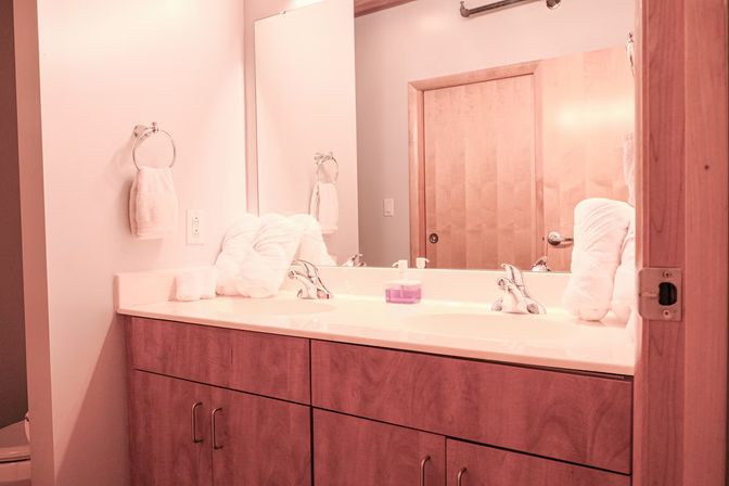 Rustic wooden double-sink bathroom vanity with chrome faucets, white folded towels, purple soap jar, large mirror and sliding wood door under warm lighting