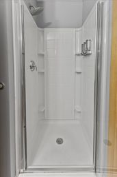 Spotless white shower stall with glass door, overhead rain showerhead, recessed corner shelves, floor drain and wall-mounted soap/shampoo dispensers — modern bathroom shower.