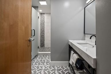 Contemporary gray bathroom interior with geometric patterned floor tiles, frosted glass walk-in shower with mosaic accent strip, white marble rectangular sink on a black metal vanity and matte black faucet