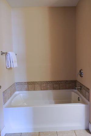 White alcove bathtub with beige tile trim and mosaic border, chrome faucet and towel bar holding folded white towels against neutral beige bathroom walls and tiled floor