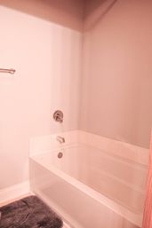 Cozy white alcove bathtub with chrome faucet and single-handle control, towel bar on a pale wall and a gray bath mat in a modern residential bathroom.