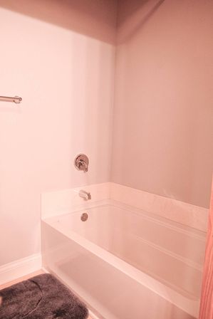 Cozy white alcove bathtub with chrome faucet and single-handle control, towel bar on a pale wall and a gray bath mat in a modern residential bathroom.