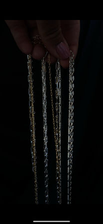 Close-up of a hand holding multiple gold and silver chain necklaces against a dark background, showcasing varied link styles.