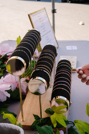 Colorful and gold chain bracelets on black velvet display rods at an outdoor market stall, hand with white manicure selecting one