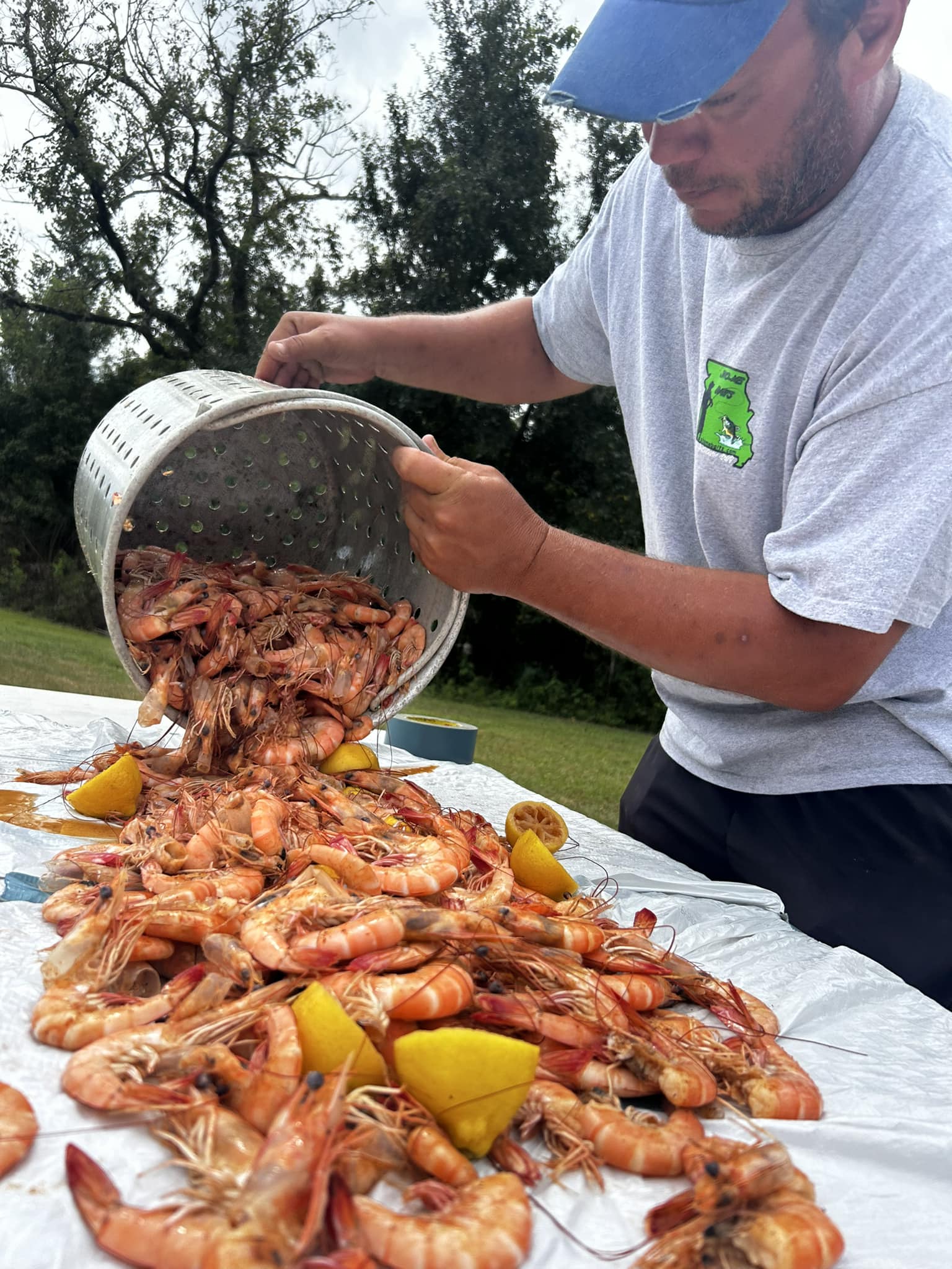 Outdoor shrimp boil: bright orange shell-on shrimp and lemon wedges poured from a perforated pot onto a picnic table.