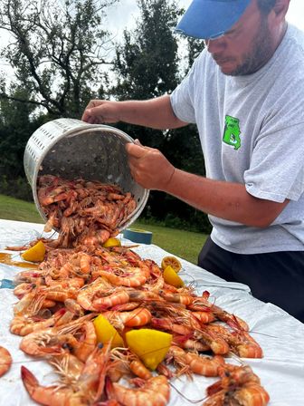 Outdoor shrimp boil: bright orange shell-on shrimp and lemon wedges poured from a perforated pot onto a picnic table.