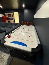 Cozy home basement game room with white air hockey table, foosball, gray sectional sofa, red mini fridge, dark gray walls and sliding barn door