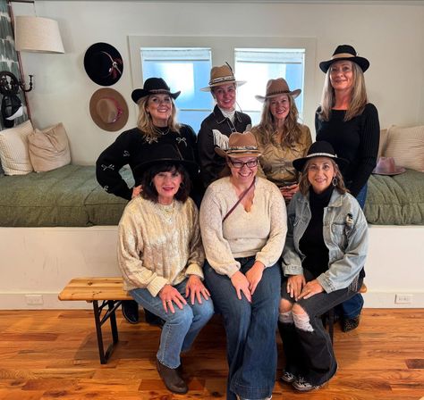 Seven women wearing cowboy hats smile for a group photo inside a cozy western hat boutique with a wooden bench, built-in daybed and warm hardwood floor.