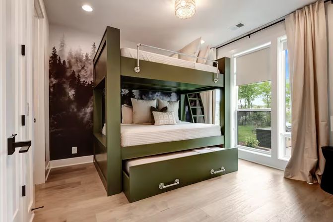 Sunlit modern bedroom with olive-green bunk bed and pull-out trundle, forest mural accent wall, hardwood floors and large floor-to-ceiling window.